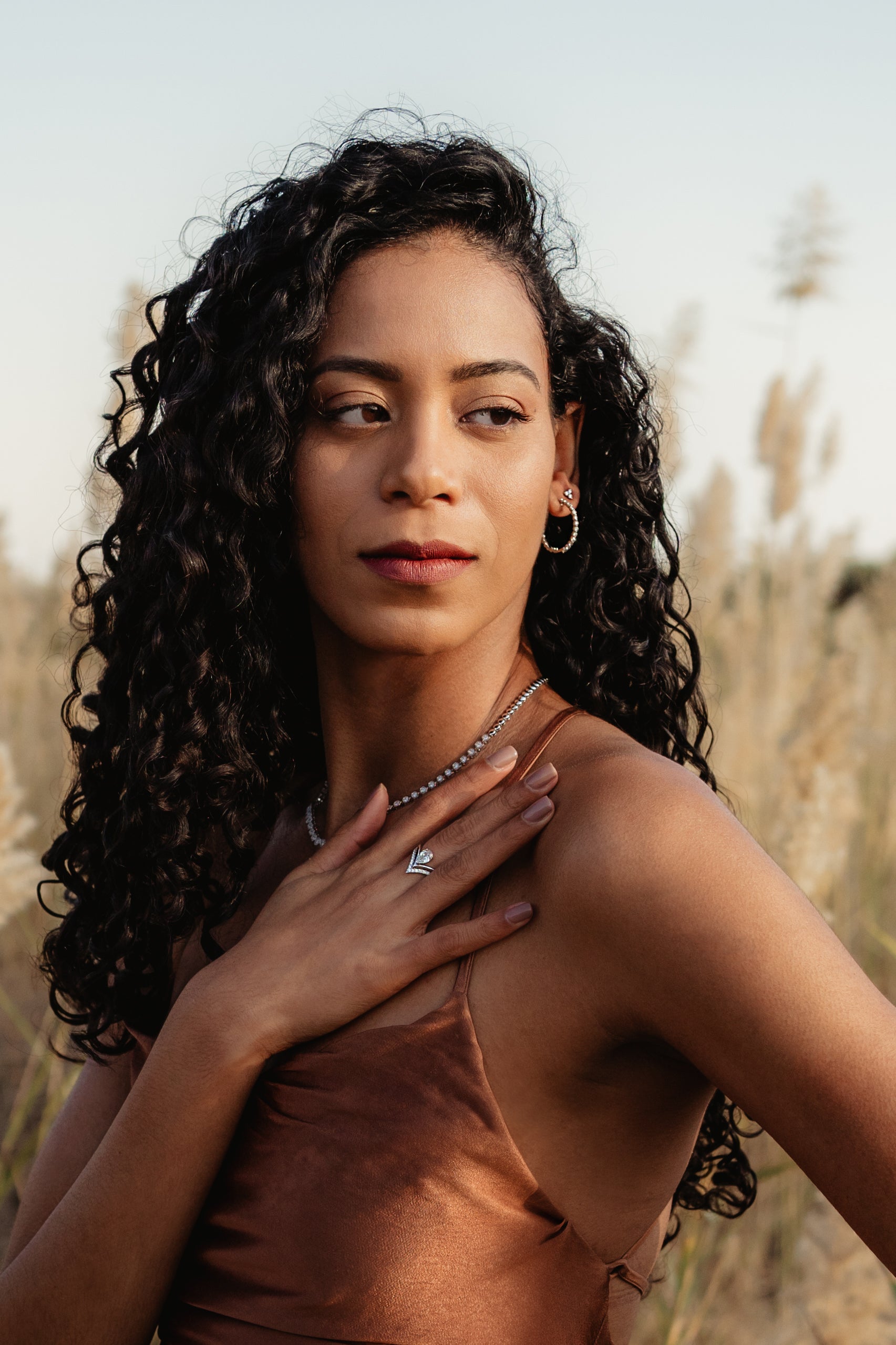 Woman with long curly hair wearing Saint Stone jewelry, standing in a field of tall grass, Australian luxury jewelry brand photoshoot