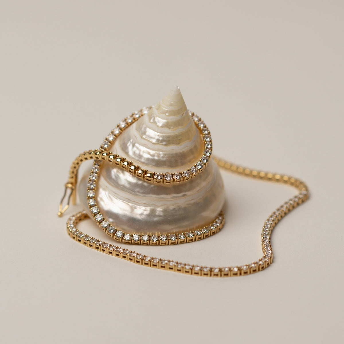 Shell-shaped handbag with a gold chain on a beige background by Saint Stones.