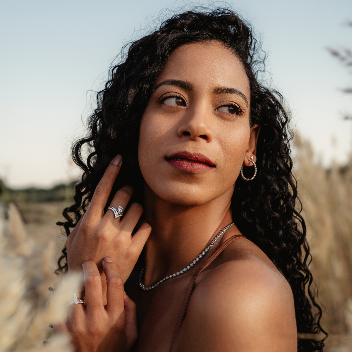 Woman modelling wishbone diamond engagement ring, diamond tennis necklace, and diamond hoop earring with a desert background