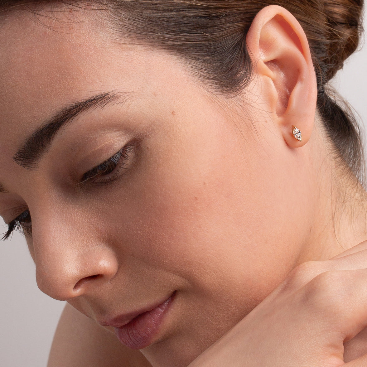 Close-up of a woman wearing a diamond stud earring on a neutral background