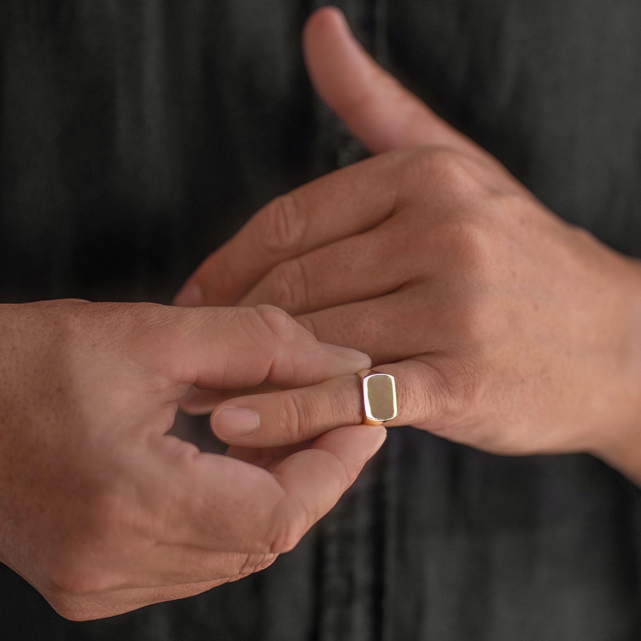 Close-up of two hands with one wearing a gold ring on a dark background