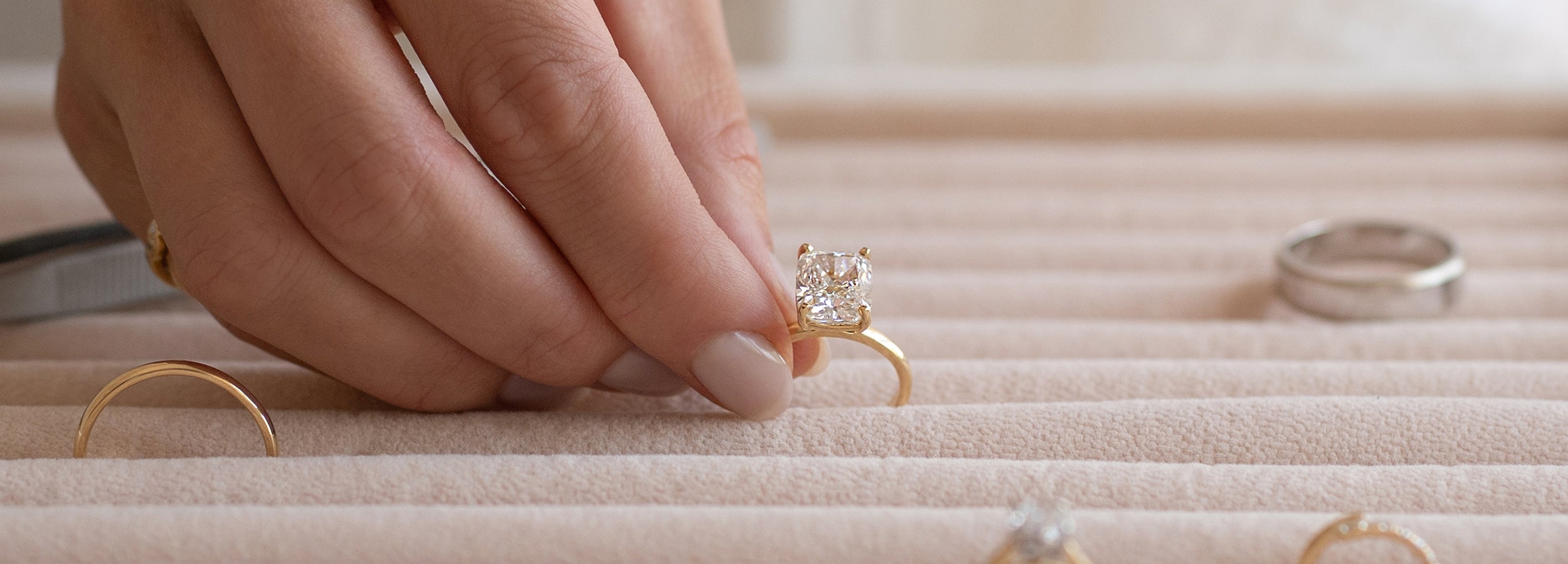 Hand holding a diamond ring over a jewelry box with other rings by Saint Stones.